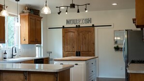 Una cocina con armarios de madera, una isla central, iluminación colgante y un letrero con la palabra 'NOURISH'.