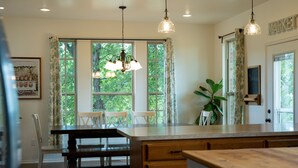 Una cocina con isla de madera, luces colgantes y amplias ventanas con cortinas.