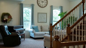 Una sala de estar con un piano, un sofá, una escalera y un reloj de pared.