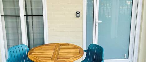A patio with a round wooden table and two blue chairs, a sliding glass door, and a brick wall.