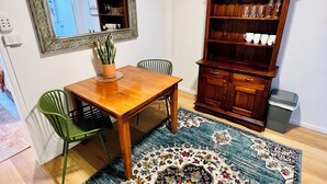 A dining area with a wooden table, two chairs, a rug, a mirror, and a wooden cabinet with glassware. - City Unit 5 Walk to Esplanade (Cairns North)