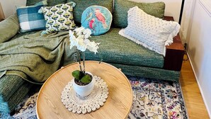 A cozy living room with a green sofa, a round wooden coffee table with a white orchid, and a colorful patterned rug. - City Unit 5 Walk to Esplanade (Cairns North)