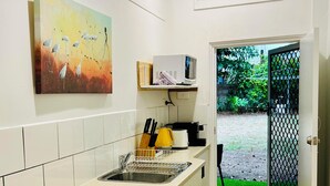A compact kitchen with white cabinets, a stove, and a microwave. There's a painting on the wall and a door leading outside. - City Unit 5 Walk to Esplanade (Cairns North)