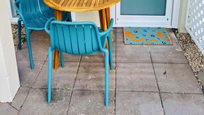 A patio with a round wooden table and two blue chairs, a door with a frosted glass panel, and a small outdoor light fixture. - City Unit 5 Walk to Esplanade (Cairns North)