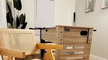 A chessboard set up on a table in a room with a wooden cabinet, a rattan chair, and a window with blinds.