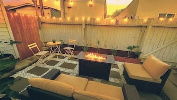 A patio with a fire pit, outdoor furniture, and string lights.