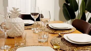 A dining table set with plates, glasses, and cutlery, surrounded by woven placemats and a large plant.