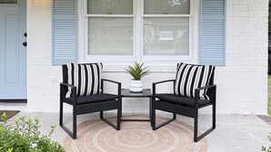 Eine Veranda mit zwei schwarzen Korbstühlen, einem kleinen Tisch und einem Blumentopf.