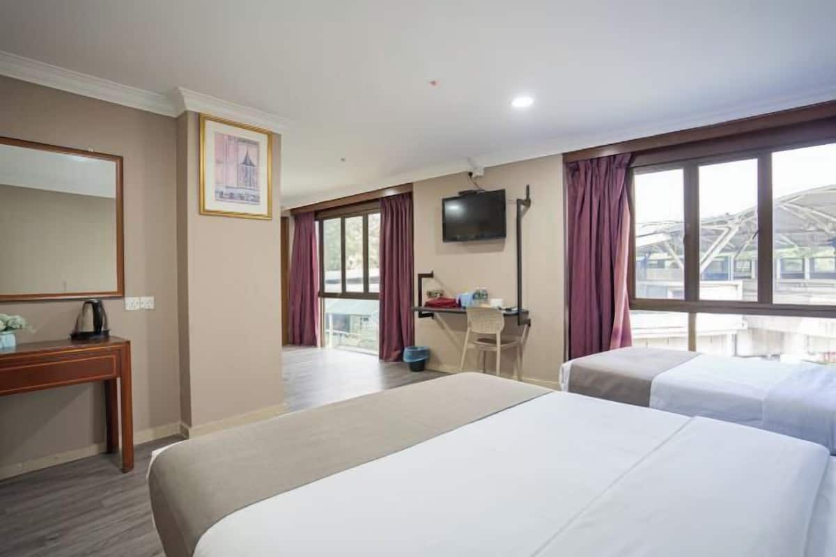 A hotel room with two beds, a desk, a chair, a TV, and a large window with curtains.