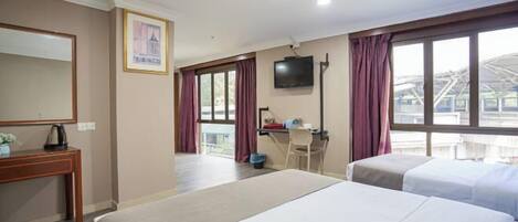 Habitación de hotel con dos camas, un escritorio, una silla, un televisor y un amplio ventanal con cortinas.