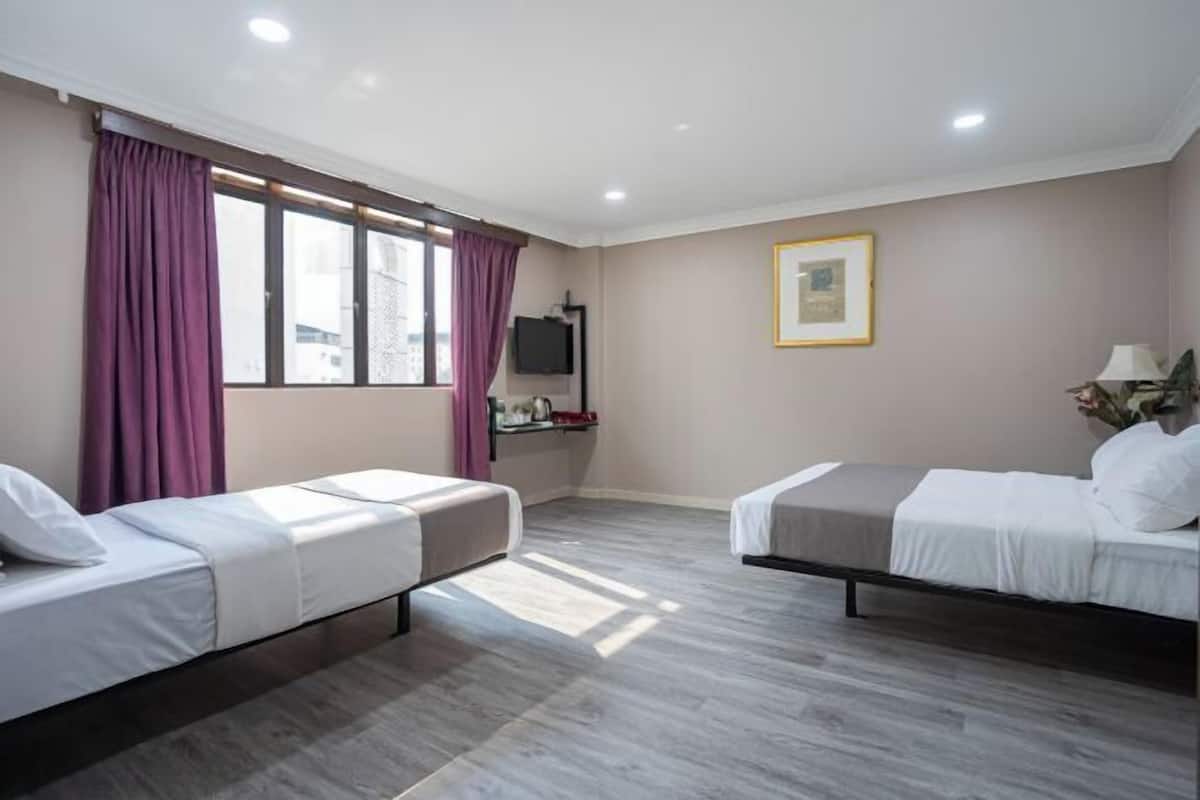 A hotel room with two single beds, a television, a framed picture on the wall, and a window with curtains.