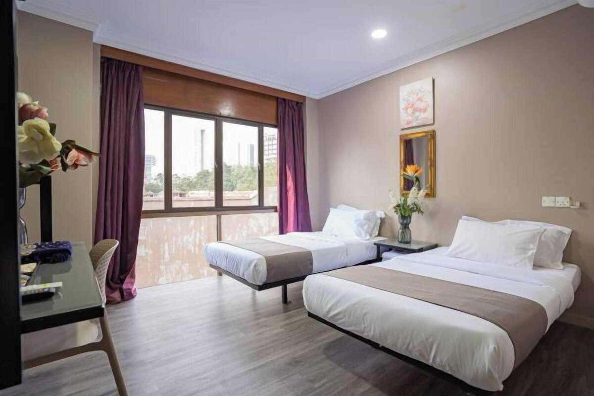 A hotel room with two beds, a desk, and a large window with curtains.