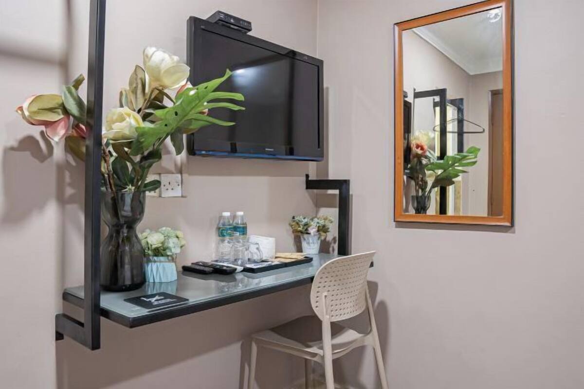 A hotel room with a desk, a flat-screen TV, a large mirror, and a chair.
