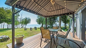 Eine überdachte Terrasse im Freien mit Blick auf den See, Holzstühle, ein Tisch und Lichterketten.