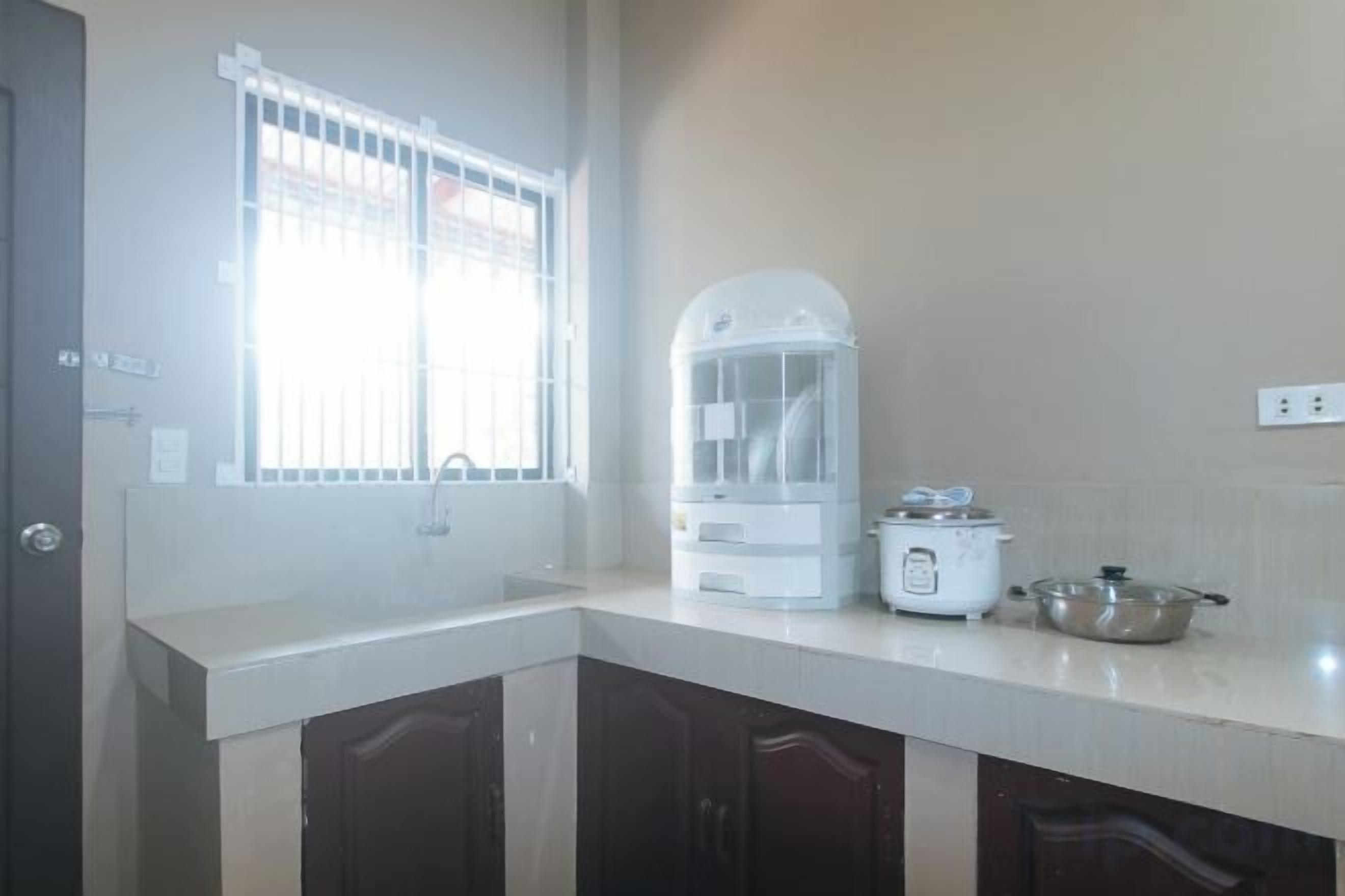 A kitchen with a window, a dish rack, a rice cooker, and a pot on the counter.