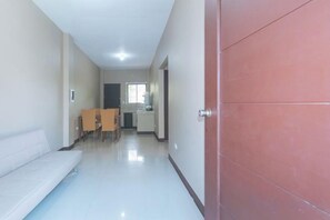 A hallway with a dining area, a sofa, and a red door. - RedDoorz @ Aurea Apartelle (Iloilo City)