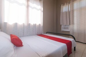 A single bed with a white and red bedspread, a red pillow, and a window with sheer curtains. - RedDoorz @ Aurea Apartelle (Iloilo City)