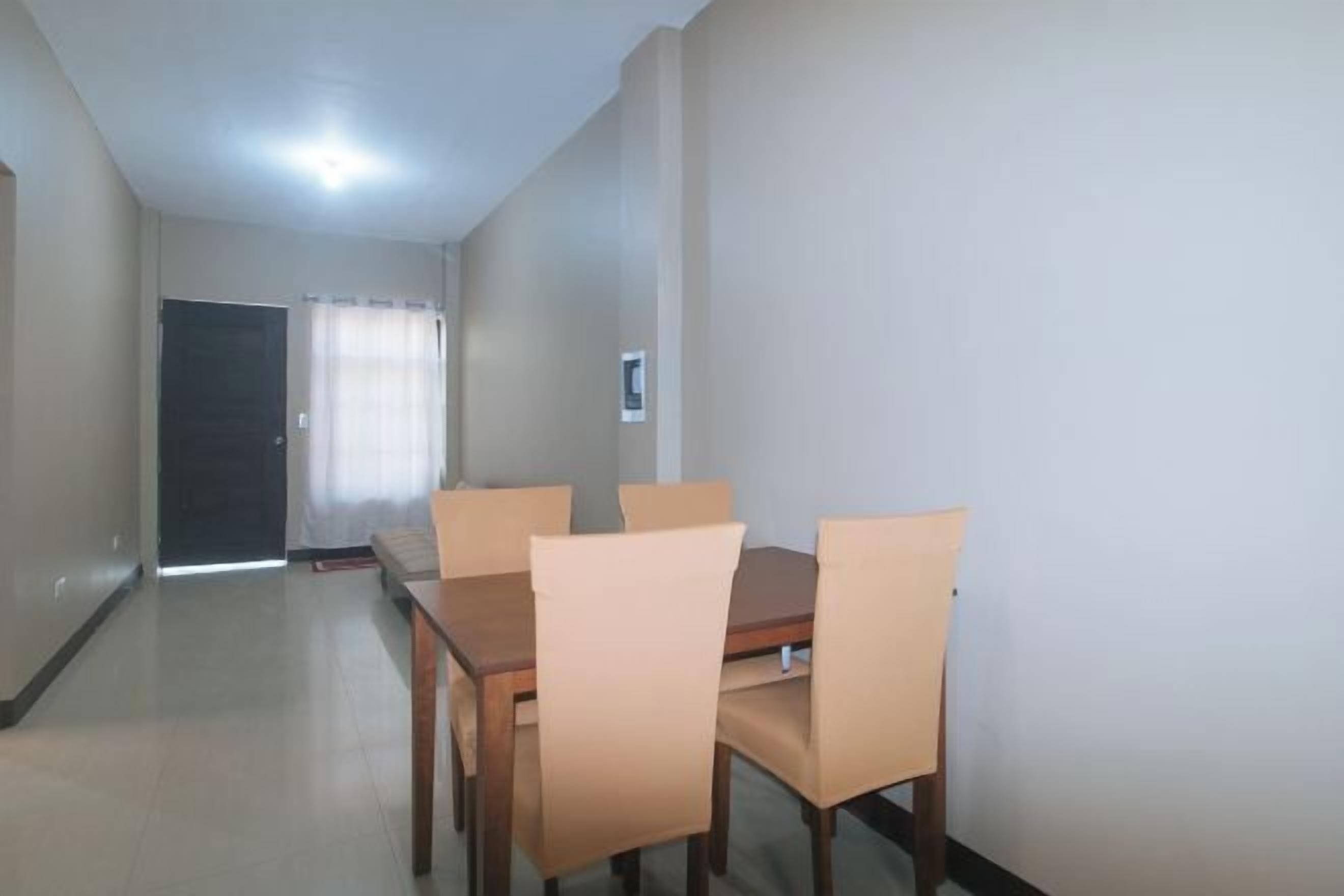 A dining area with a wooden table and four chairs, a door, and a light switch on the wall.