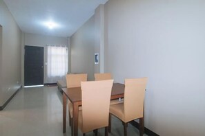 A dining area with a wooden table and four chairs, a door, and a light switch on the wall. - RedDoorz @ Aurea Apartelle (Iloilo City)