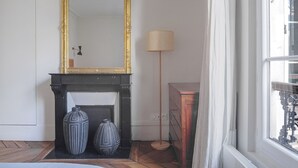 A room with a fireplace, a large mirror, two vases, a lamp, and a wooden dresser. - Blueground | Saint Vincent de Paul, view, nr Canal (Paris)