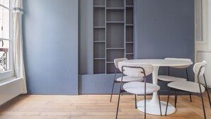 A room with a white table and chairs, a grey shelving unit, and a window with curtains. - Blueground | Saint Vincent de Paul, view, nr Canal (Paris)