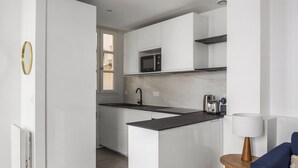 A modern kitchen with white cabinetry, a black countertop, and a microwave. There is a window above the sink and a lamp on a wooden side table.