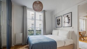 A bedroom with a large bed, a window with curtains, and two framed artworks on the wall.