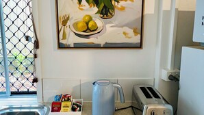 Een keuken met een spoelbak, een waterkoker, een broodrooster en een lijst met een schilderij van bloemen en citroenen aan de muur.