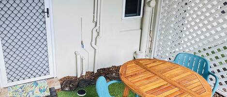 A patio with a wooden table and blue chairs, surrounded by artificial grass.