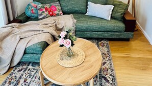 Een gezellige woonkamer met een groene bank, een ronde houten salontafel en een vloerkleed met bloemenprint.