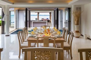 A dining area with a table set for six, overlooking a pool and a view of the sea. - Baan Ban Buri (Koh Samui)