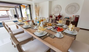 A dining table set with white plates, napkins, and various dishes, including fruits and bread, in a modern hotel room with a view of the outdoors. - Baan Ban Buri (Koh Samui)