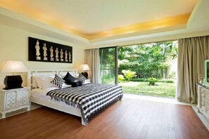 A bedroom with a large bed, two bedside tables, a television, and a view of a garden. - Baan Ban Buri (Koh Samui)