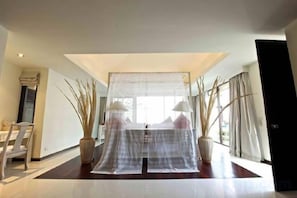 A modern hotel room with a bed covered by a sheer curtain, a large window, and a potted plant. - Baan Ban Buri (Koh Samui)