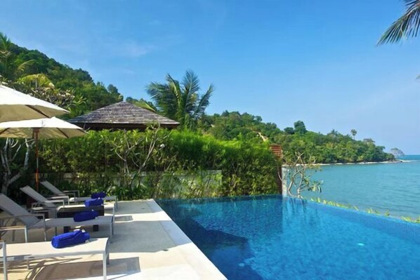 A swimming pool with lounge chairs and umbrellas, surrounded by lush greenery and a view of the sea. - Baan Ban Buri (Koh Samui)