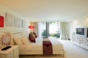 A hotel room with a bed, bedside table, lamp, TV, and a view of greenery outside. - Baan Ban Buri (Koh Samui)