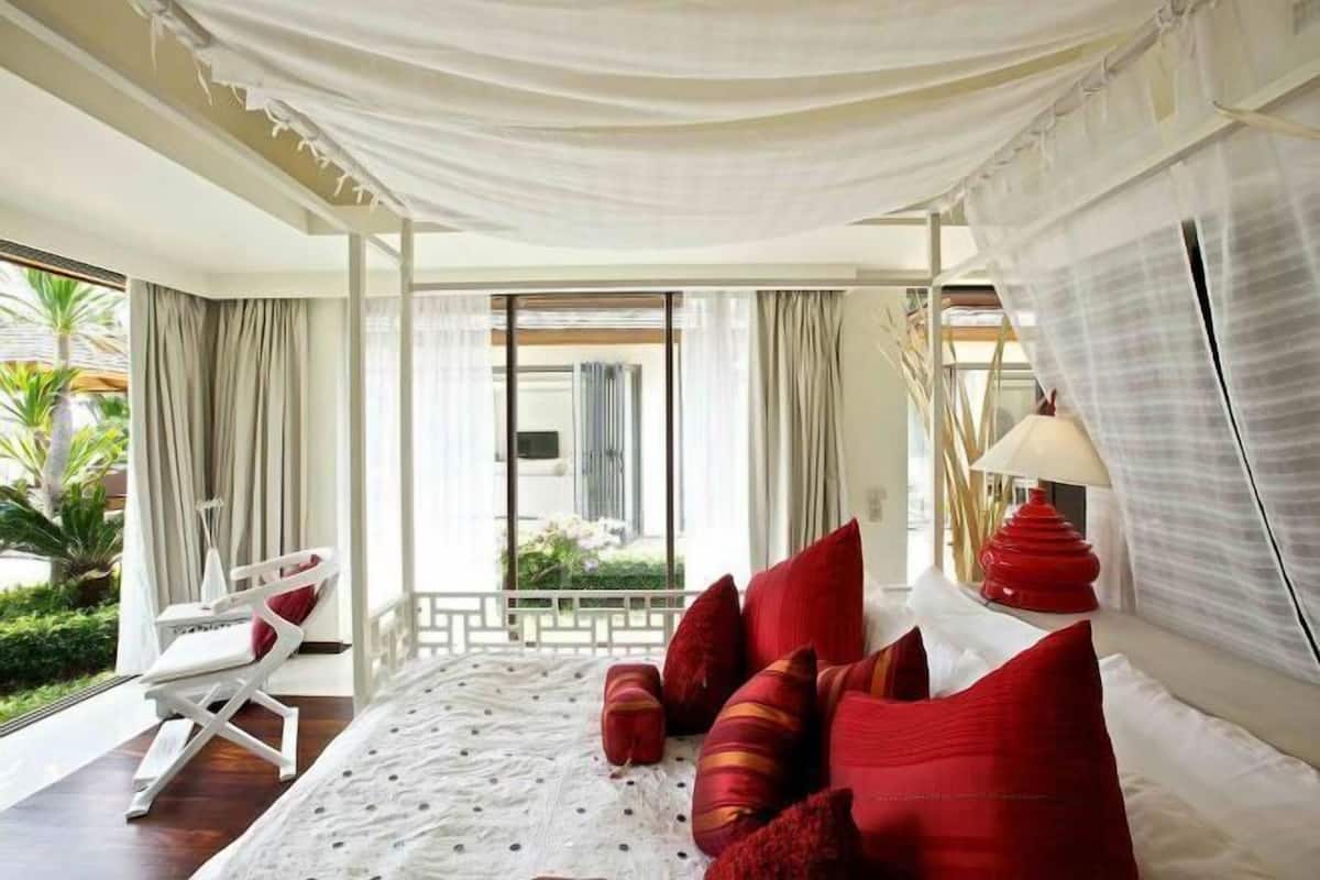 Une chambre à coucher avec un lit, des oreillers rouges, un baldaquin blanc et une vue sur la verdure à l’extérieur.