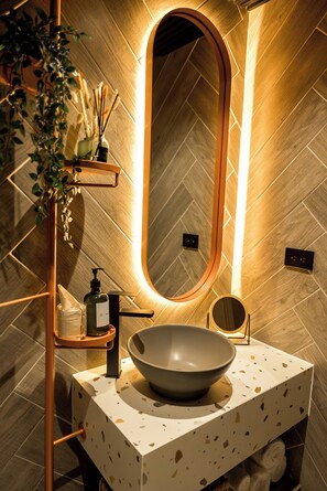 A modern bathroom with a large oval mirror, a bowl sink, a towel rack, and a plant. - Terrario las acacias  (Armenia)