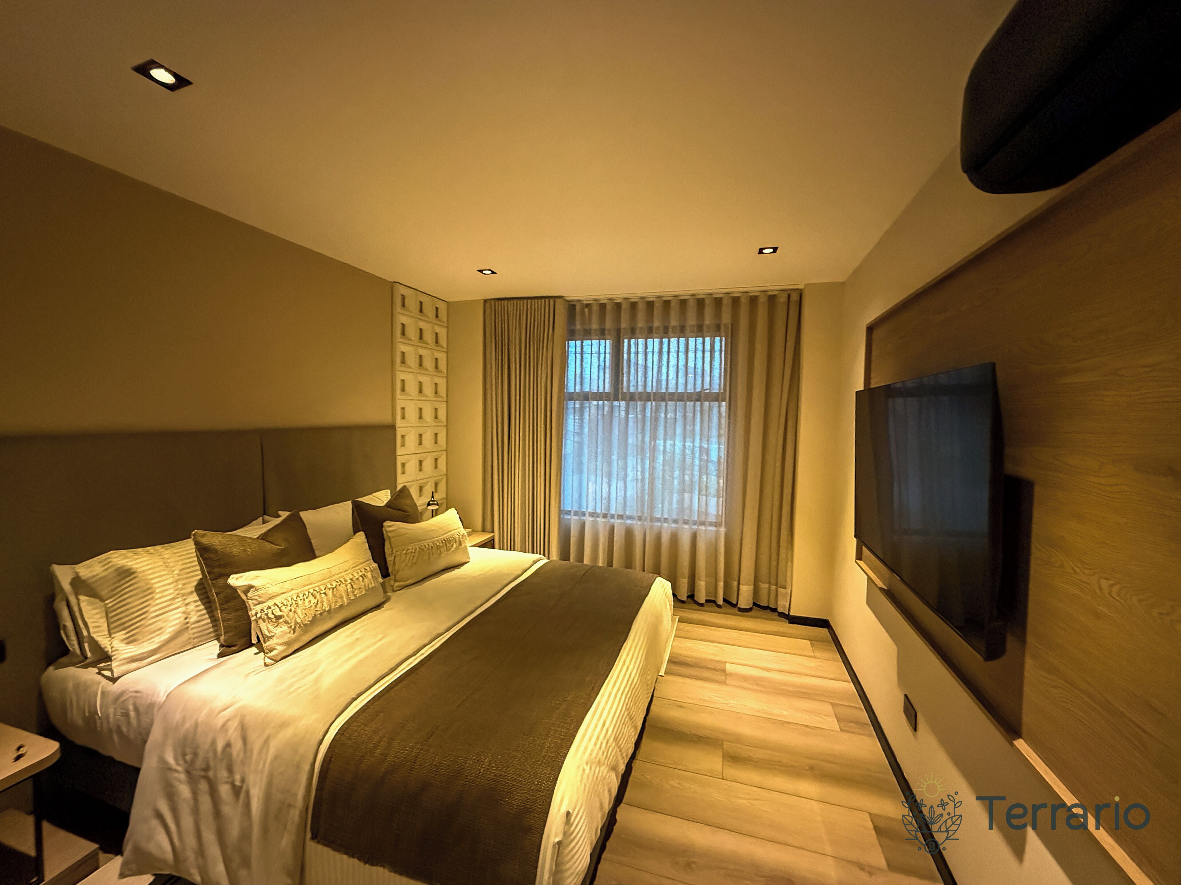 A modern bedroom with a large bed, a TV mounted on the wall, and a window with curtains.