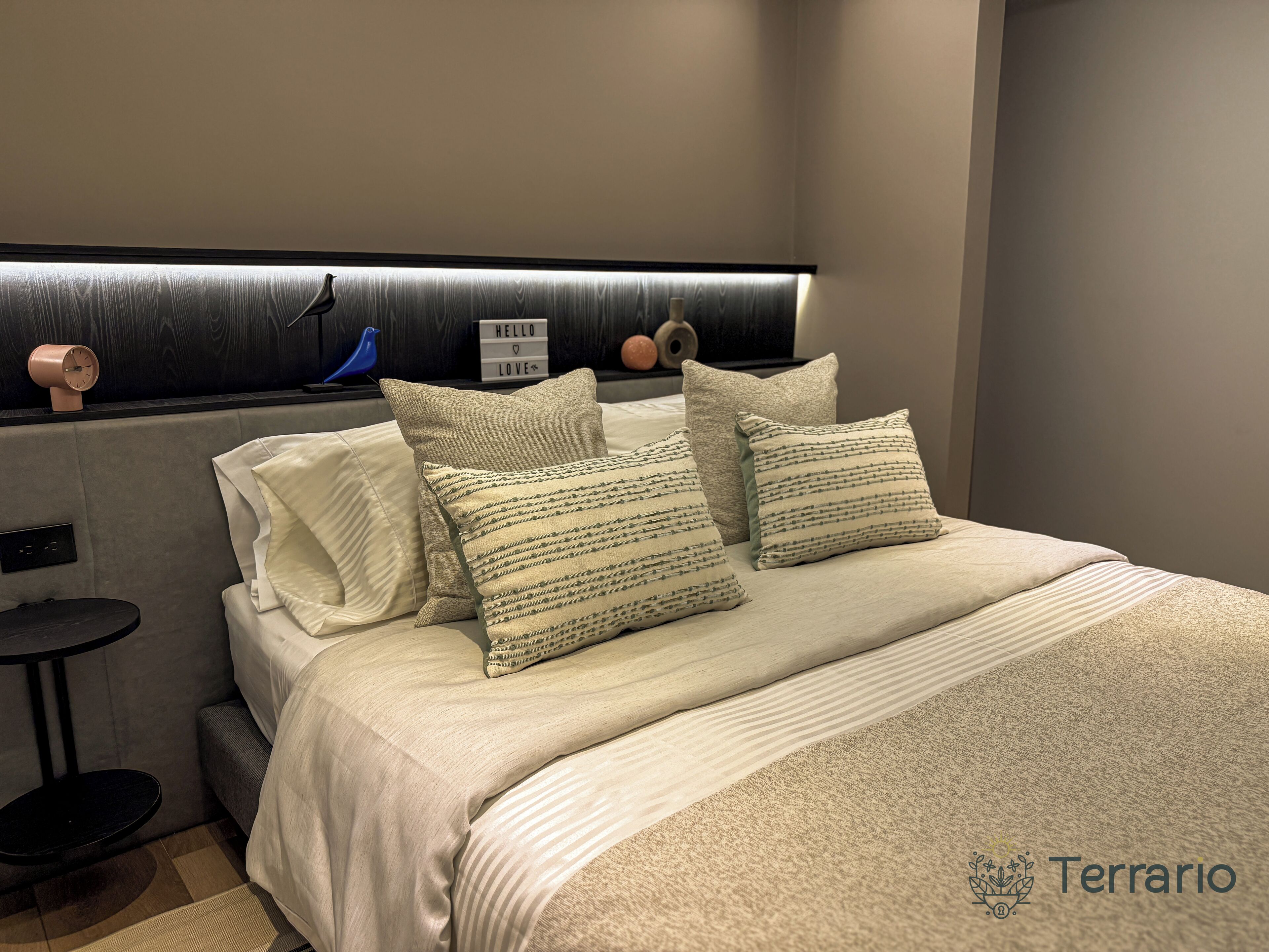 Un dormitorio moderno con cama, almohadas, mesita de noche y un reloj en la pared.