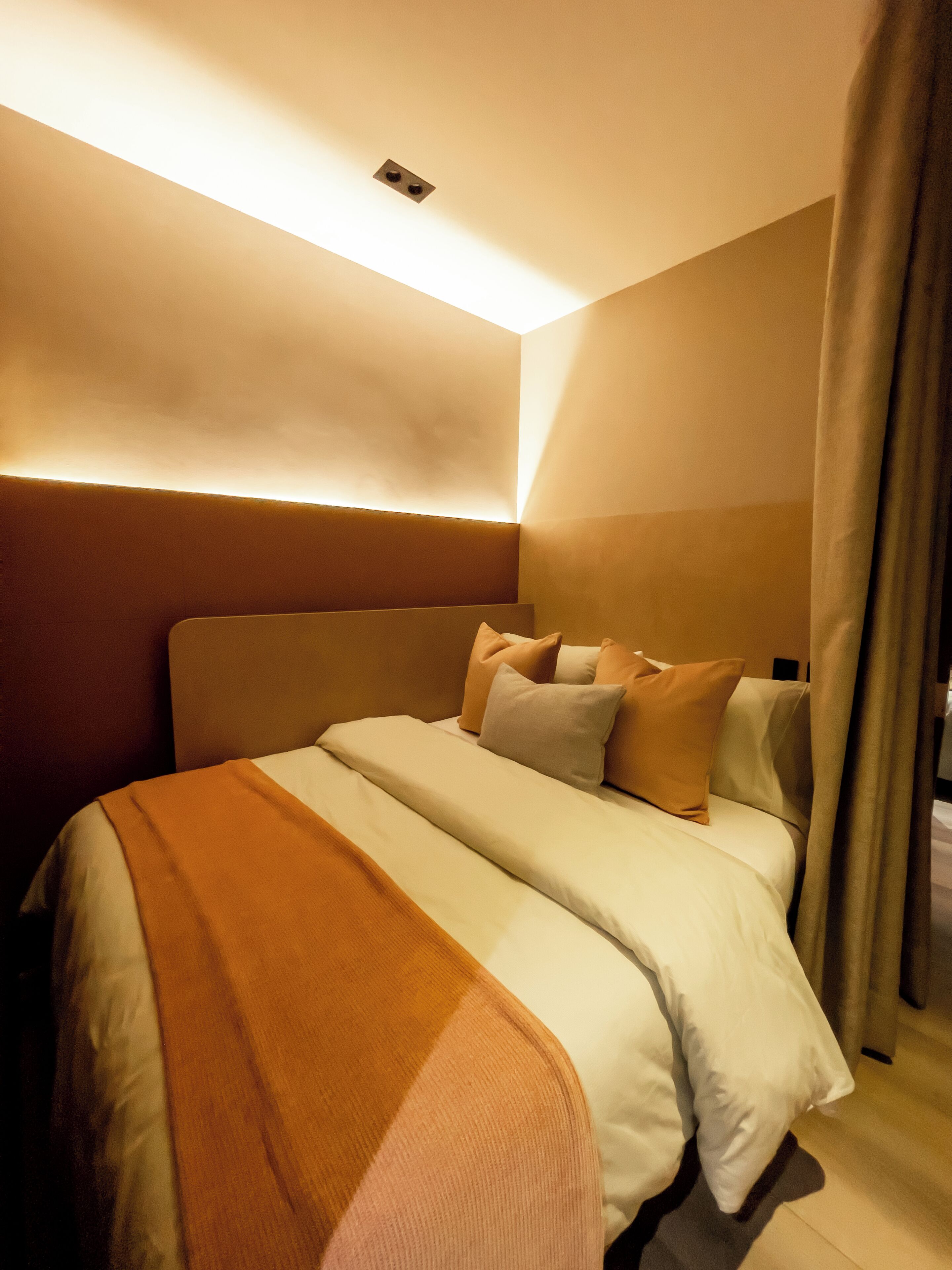 A modern hotel room with a large bed, a headboard, and a ceiling light fixture.