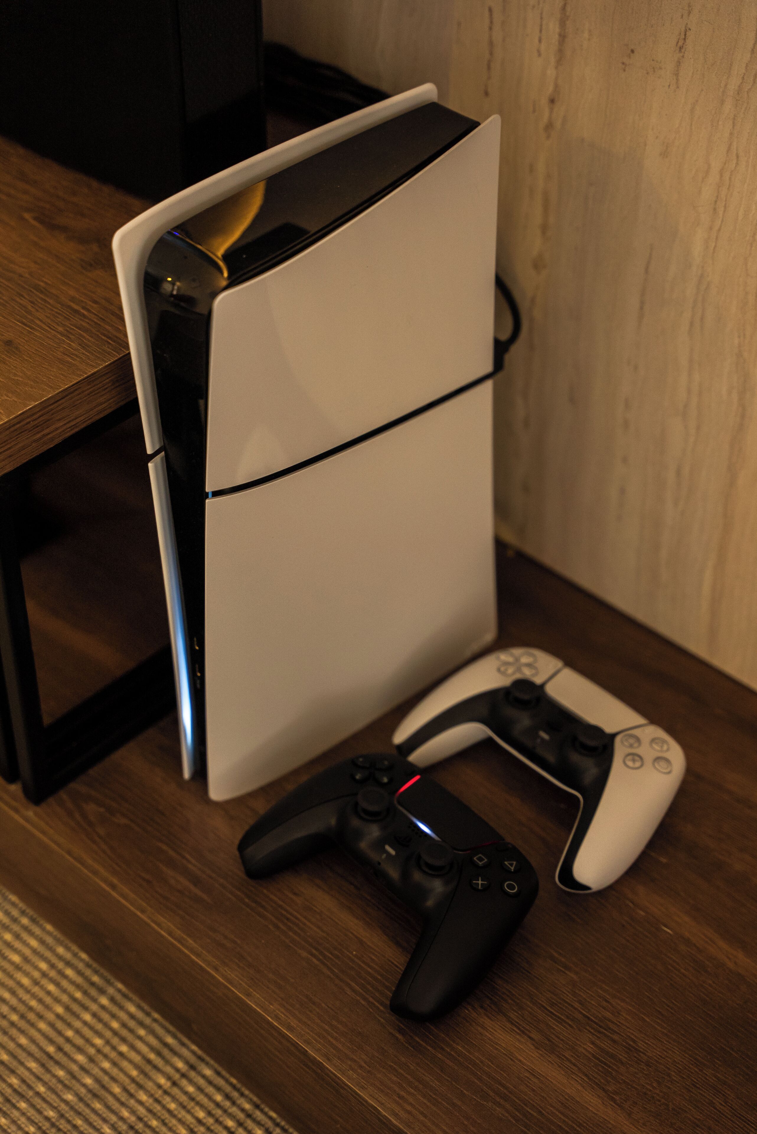 A white gaming console with a controller on a wooden surface.