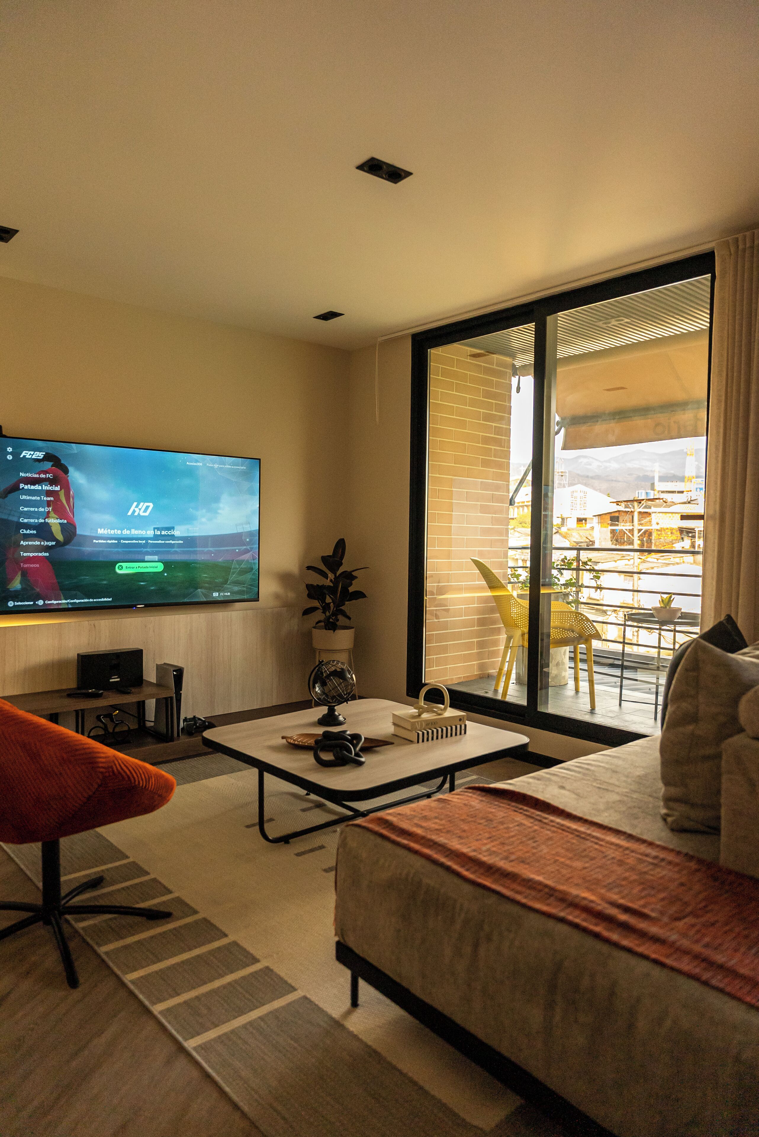 Een moderne woonkamer met een flatscreen televisie, een bank, een bijzettafeltje en uitzicht op een balkon.