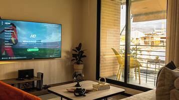 Een moderne woonkamer met een flatscreen televisie, een bank, een bijzettafeltje en uitzicht op een balkon.