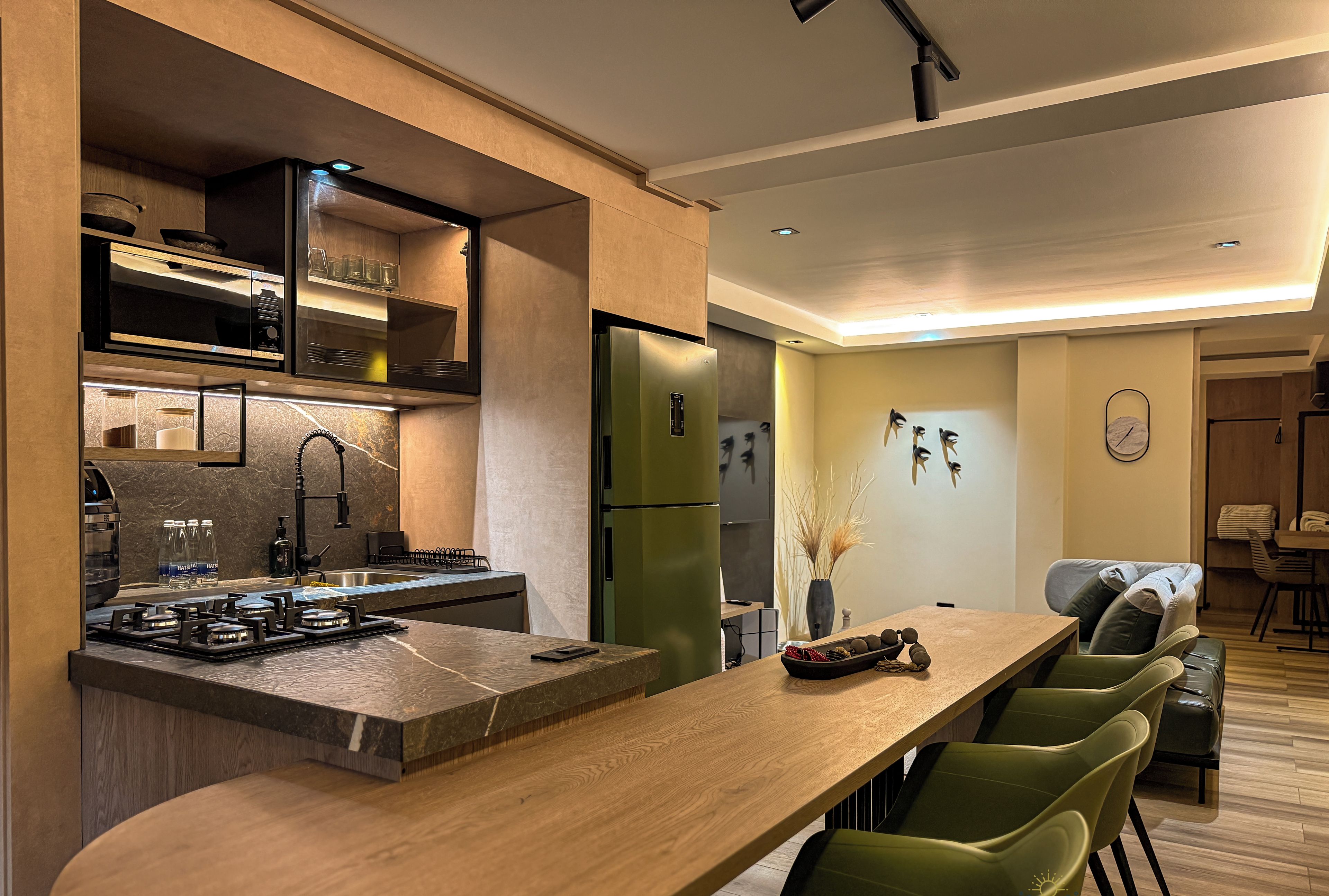 A modern kitchen with a central island, built-in appliances, and a dining area with green chairs.