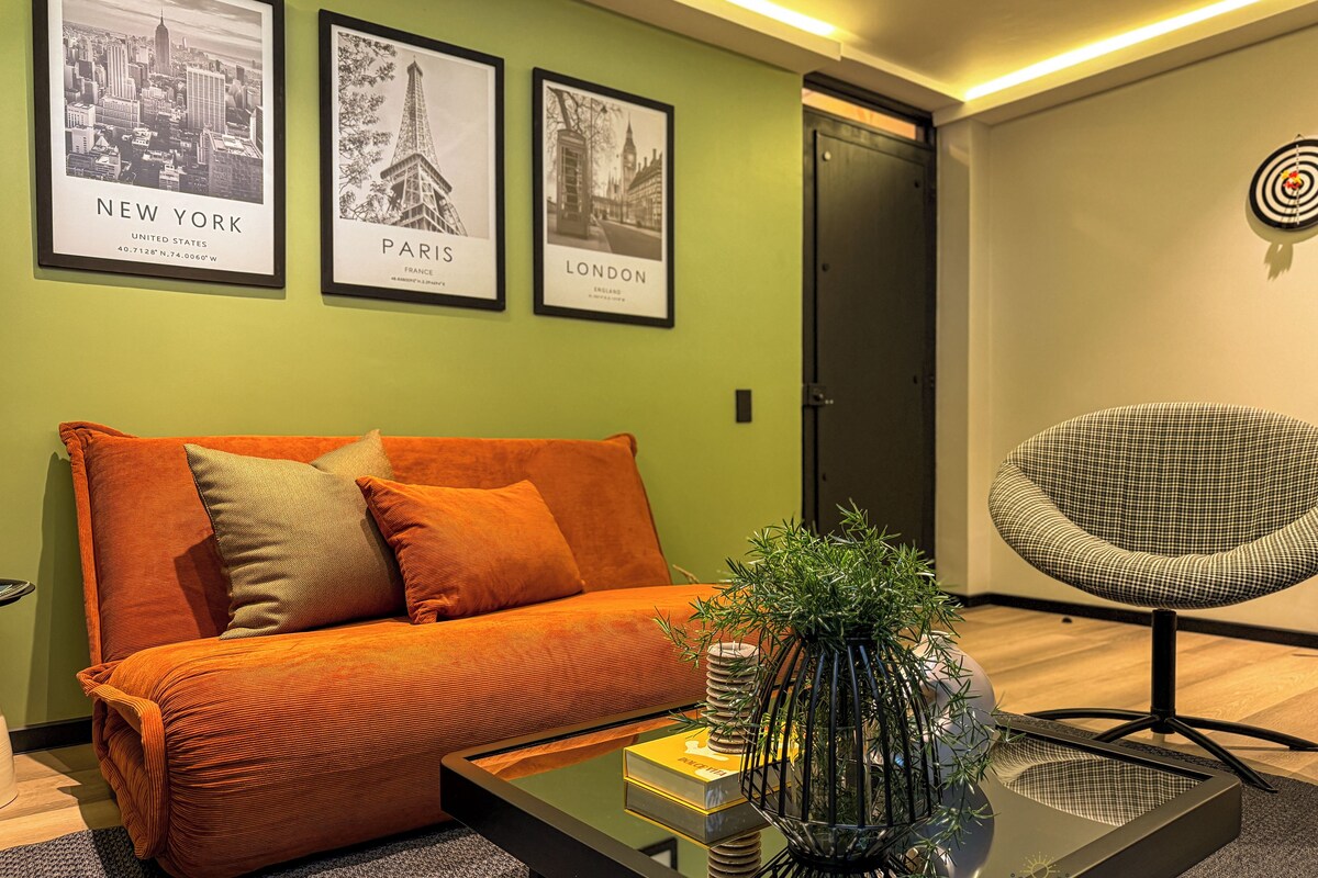 A modern living room with a sofa, a coffee table, and a chair. There are three framed pictures on the wall, one of New York, one of Paris, and one of London.