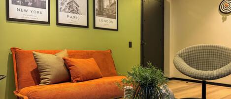 A modern living room with a sofa, a coffee table, and a chair. There are three framed pictures on the wall, one of New York, one of Paris, and one of London.