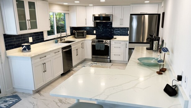 A modern kitchen with white cabinetry, a black backsplash, stainless steel appliances, and a marble countertop. - Waterfront Oasis w/heated Pool Dock Kayaks Fishing (New Port Richey)