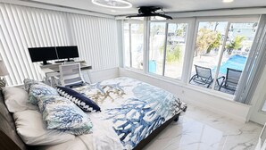 A modern bedroom with a large bed, a TV, and a view of a pool and outdoor area. - Waterfront Oasis w/heated Pool Dock Kayaks Fishing (New Port Richey)
