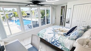 A bedroom with a large window, a bed with a marine-themed bedspread, a desk, and a chair. - Waterfront Oasis w/heated Pool Dock Kayaks Fishing (New Port Richey)